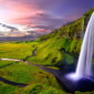 A breathtaking view of a hidden canyon in Iceland with lush green cliffs, a turquoise river, and misty mountain peaks in the background.