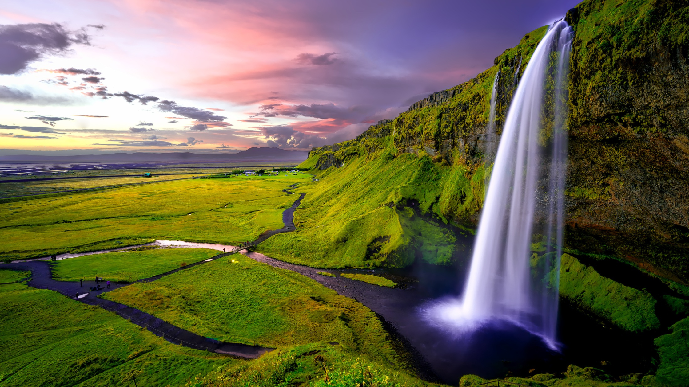 A breathtaking view of a hidden canyon in Iceland with lush green cliffs, a turquoise river, and misty mountain peaks in the background.