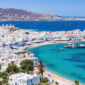 A breathtaking view of Greece featuring white-washed buildings, blue-domed churches, and the deep blue Aegean Sea under a golden sunset."