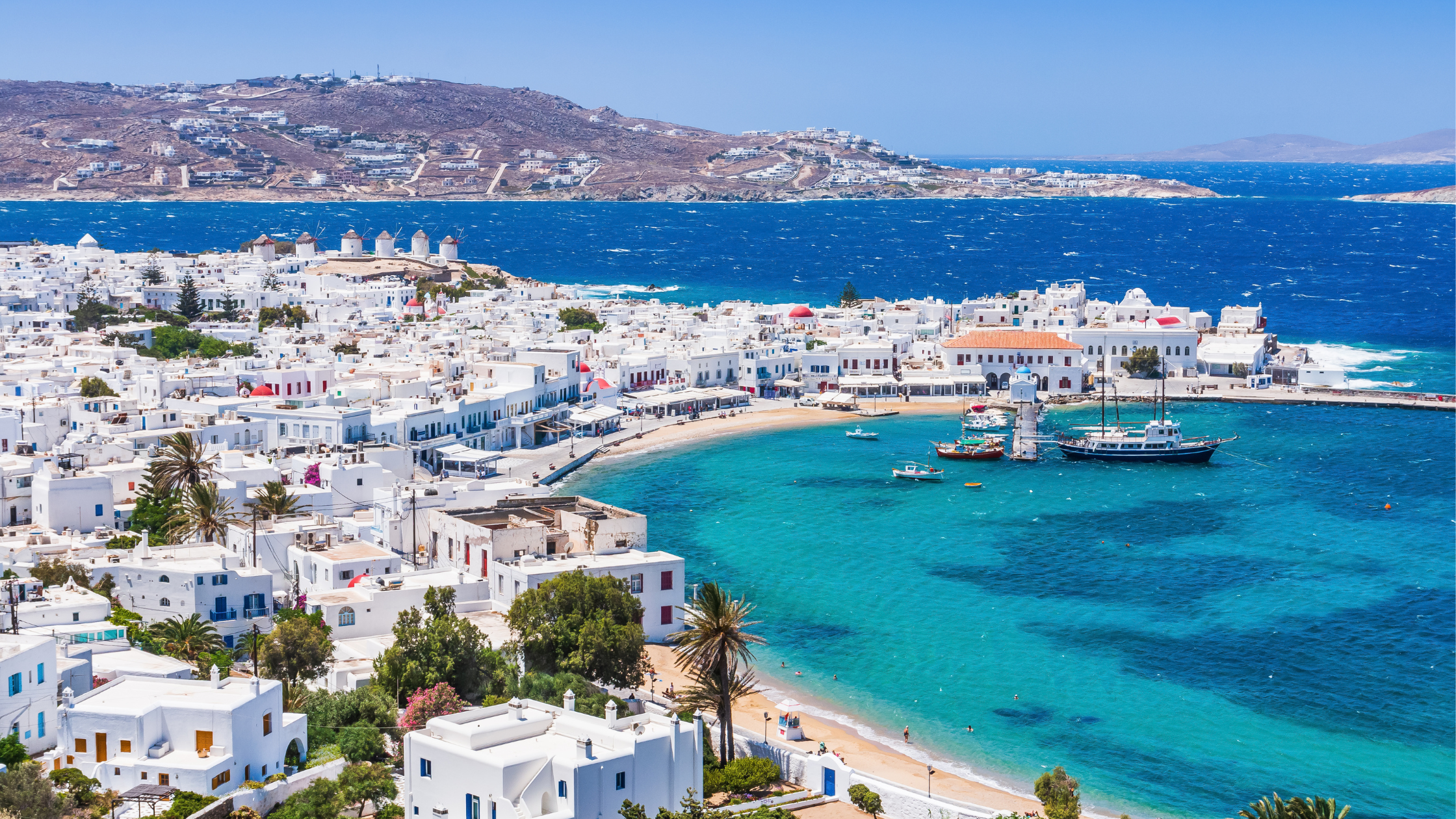 A breathtaking view of Greece featuring white-washed buildings, blue-domed churches, and the deep blue Aegean Sea under a golden sunset."